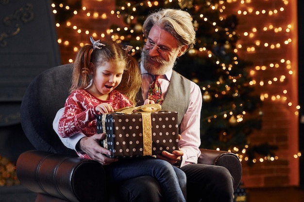 Uomo anziano dallo stile allegro con capelli grigi e barba con bambina con confezione regalo.