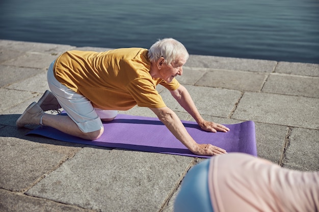 uomo anziano e il suo compagno di yoga che fanno un esercizio di allungamento della schiena