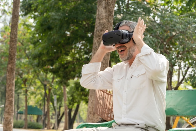 Uomo anziano eccitato guardando su occhiali VR seduto al parco