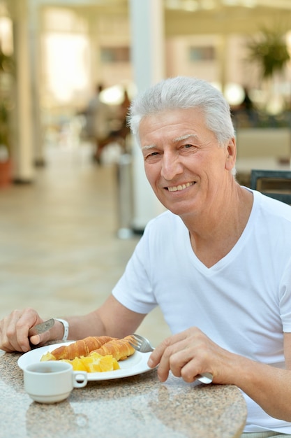 Uomo anziano felice che fa colazione al bar