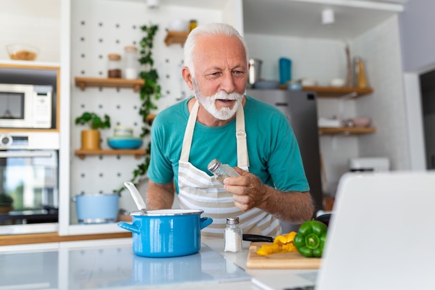 Uomo anziano felice che si diverte a cucinare a casa Persona anziana che prepara pranzo salutare in cucina moderna Tempo di stile di vita in pensione e concetto di nutrizione alimentare