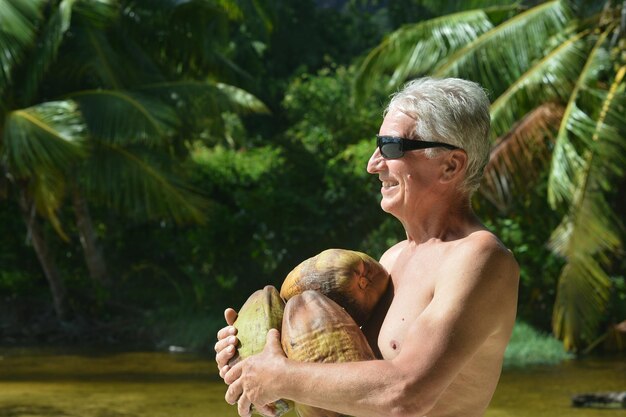 Uomo anziano felice con frutti esotici al resort tropicale