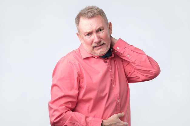 Uomo anziano frustrato in camicia rossa che tiene la mano sul collo