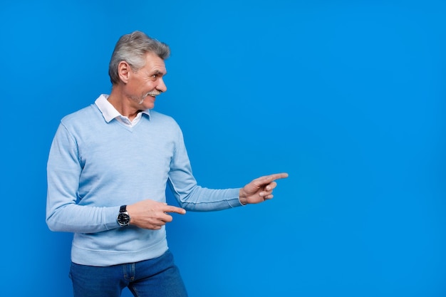 Uomo anziano in abbigliamento casual che punta a copiare lo spazio isolato sulla parete blu