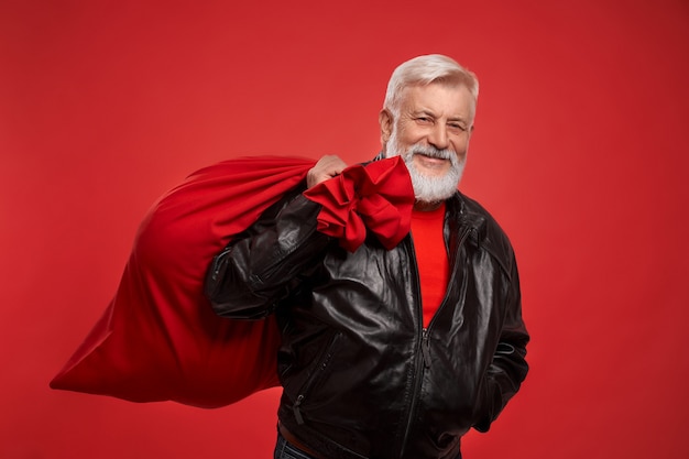 Uomo anziano in maglione rosso e giacca nera con un grande sacco di babbo natale
