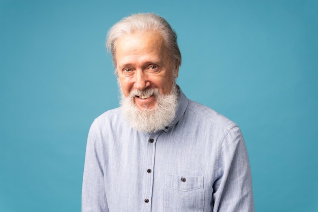 Uomo anziano in pensione con i capelli bianchi e la barba bocca aperta sorriso lucido che si diverte eccitato su sfondo blu e copia spazio