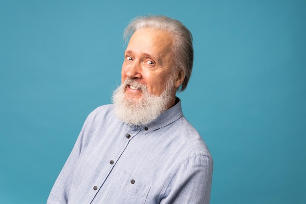 Uomo anziano in pensione con i capelli bianchi e la barba bocca aperta sorriso splendente che si diverte eccitato su sfondo di colore blu e copia spazio