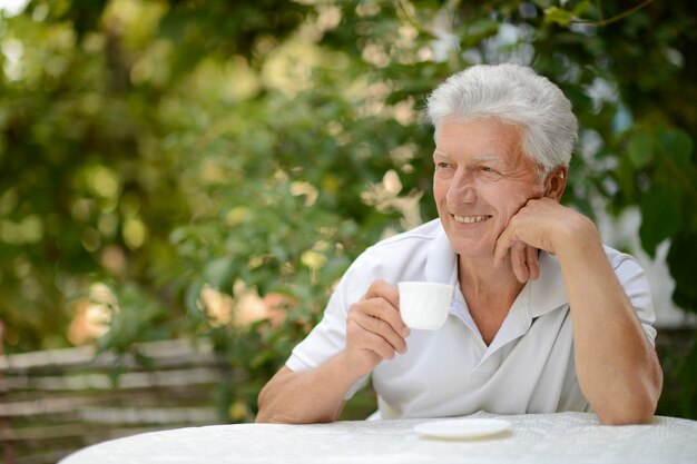 Uomo anziano in un parco estivo con una tazza di caffè