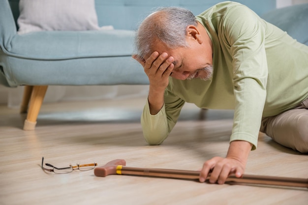 Uomo anziano mal di testa sdraiato sul pavimento dopo essere caduto dolore e dolore da osteoporosi uomo anziano caduto sul pavimento da solo con la bacchetta a casa assistenza sanitaria e medicina