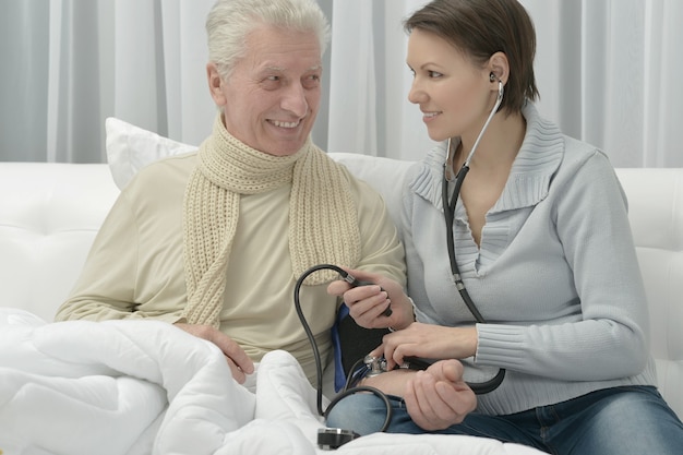 Uomo anziano malato e figlia premurosa a casa che misurano la pressione sanguigna