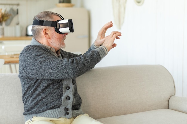 Uomo anziano maturo eccitato che indossa le cuffie con occhiali vr metaverse per realtà virtuale a casa nonno