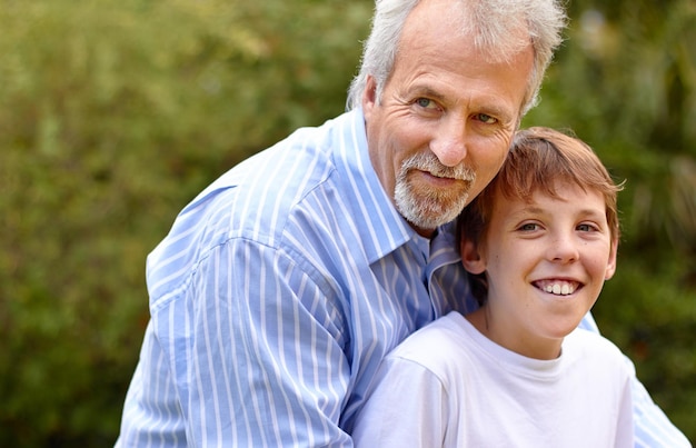 Uomo anziano o figlio con un abbraccio in natura all'aperto in un cortile di un parco o in un ambiente per il legame e la cura Famiglia padre o figlio con un abbraccio per amore supporto e relazione con felicità o sorriso