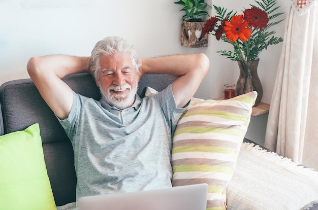 Uomo anziano rilassato sorridente seduto sul divano utilizzando il nonno del computer portatile che gode della nuova tecnologia navigando sui concetti di internet sulla comunicazione e-commerce online