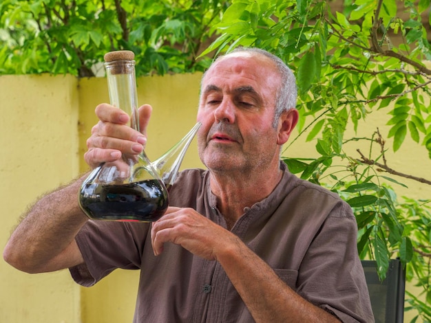 Uomo anziano seduto a un tavolo con un bicchiere di vino rosso in mano