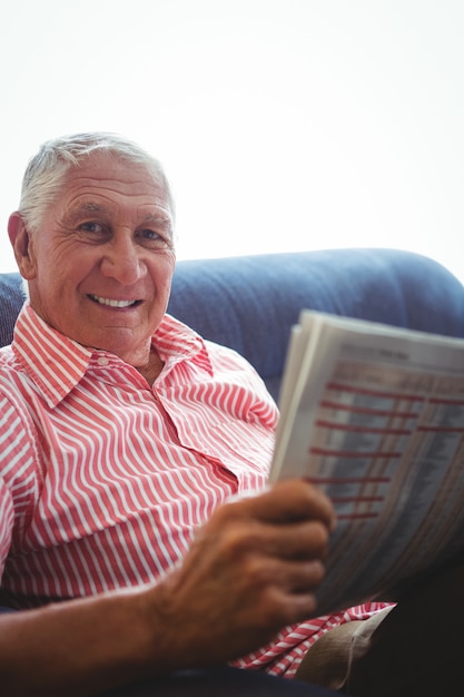 Uomo anziano seduto su un divano guardando la fotocamera mentre si tiene il giornale