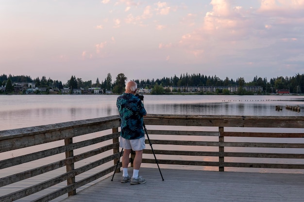 Uomo anziano senza volto che scatta foto del paesaggio sul lago al tramonto. Fotografo