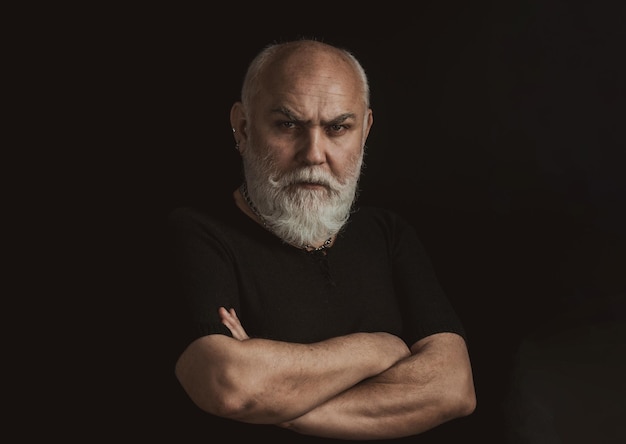 Uomo anziano serio che guarda la macchina fotografica isolata sul ritratto nero dello studio di chiave bassa del primo piano dei capelli grigi