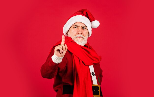 Uomo anziano serio in costume di Babbo Natale. buon anno 2021. buon Natale. santa barbuta in sciarpa su sfondo rosso. regali di Natale e tempo per lo shopping di regali. gioia delle vacanze invernali.