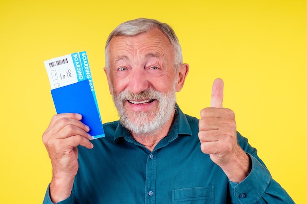 Uomo anziano sorridente che tiene passaporto in copertina blu e biglietti studio sfondo giallo.