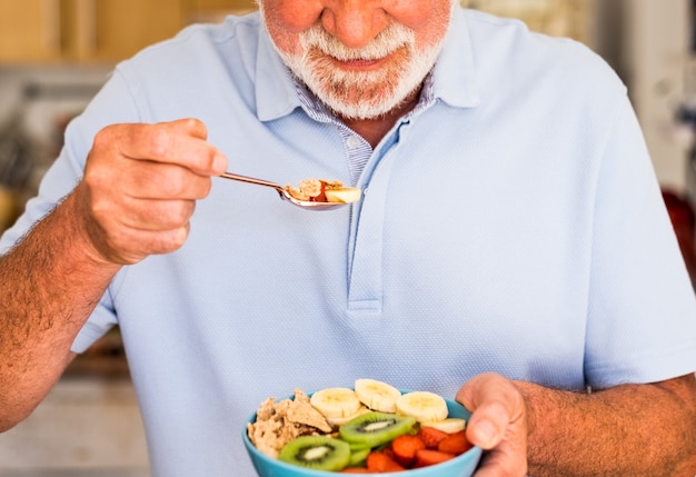 Uomo anziano sorridente che tiene una ciotola di frutta fresca e secca. Colazione o pranzo, mangiar sano