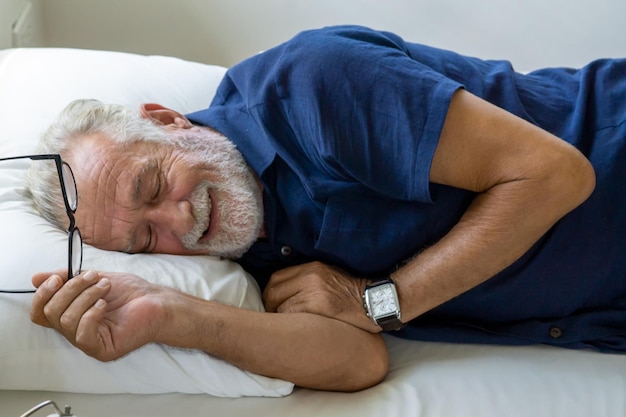Uomo anziano sorridente con gli occhiali sdraiato sul letto a casa