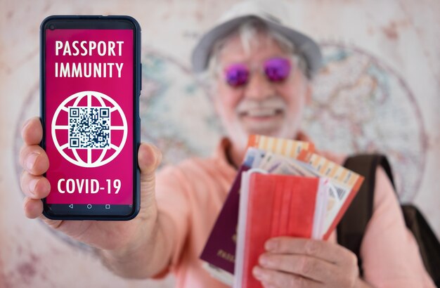 Uomo anziano sorridente sfocato che tiene in mano un pass verde sul certificato di vaccinazione del telefono cellulare