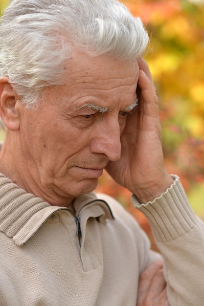 Uomo anziano triste che posa nel parco d'autunno