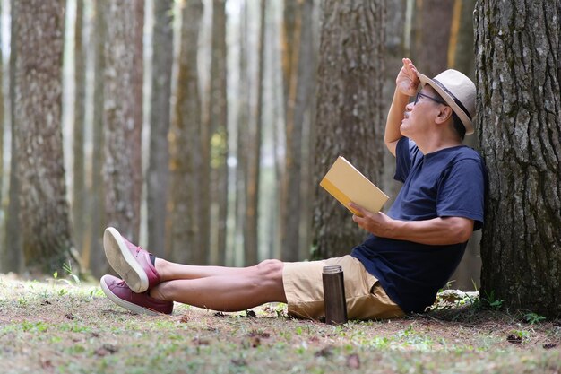 Uomo appoggiato ad un albero seduto sull'erba a leggere un libro sotto una calda giornata di sole