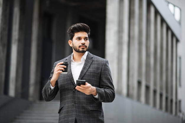 Uomo arabo che utilizza smartphone e beve caffè per strada