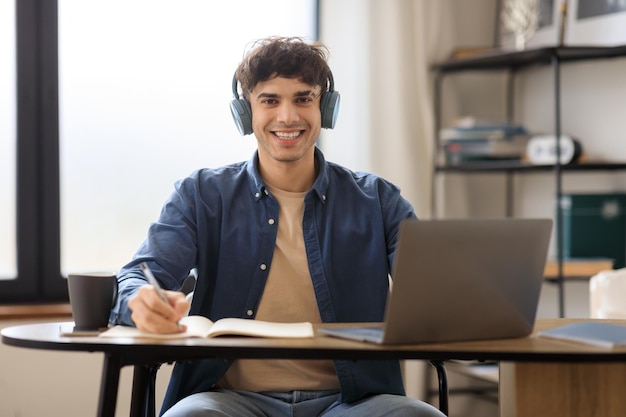 Uomo arabo che utilizza un computer portatile che prende appunti seduto al tavolo all'interno