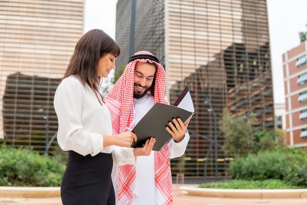 Uomo arabo felice che firma un contratto dopo la negoziazione con una donna d'affari caucasica durante una riunione all'aperto