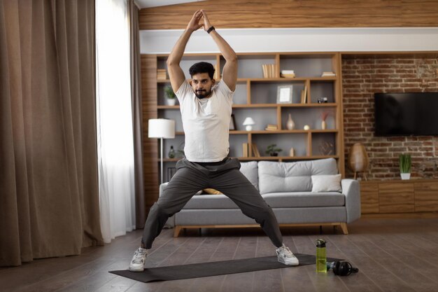 Uomo arabo in abiti sportivi che pratica yoga a casa