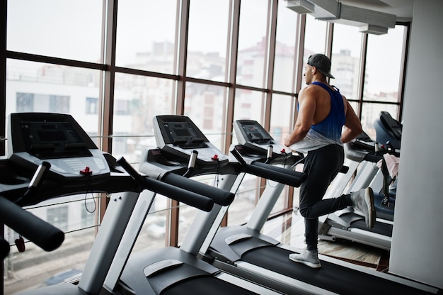 Uomo arabo in forma e muscoloso in esecuzione sul tapis roulant in palestra.