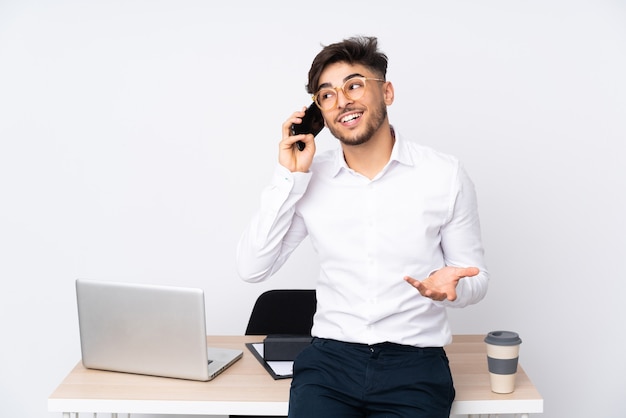 Uomo arabo in un ufficio isolato su sfondo bianco mantenendo una conversazione con il telefono cellulare con qualcuno