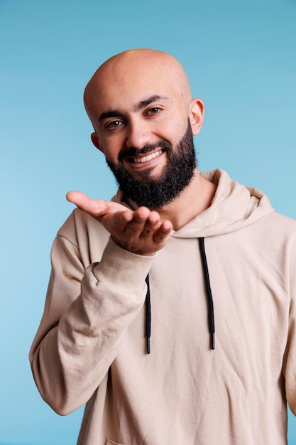 Uomo arabo sorridente che si bacia mentre guarda la telecamera con un'espressione facciale allegra. Persona felice che esprime amore e mostra affetto con emozioni gioiose ritratto in studio