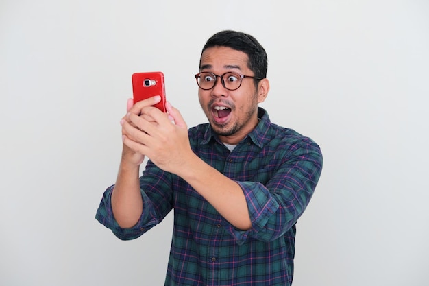 Uomo asiatico adulto che guarda al suo handphone con espressione wow