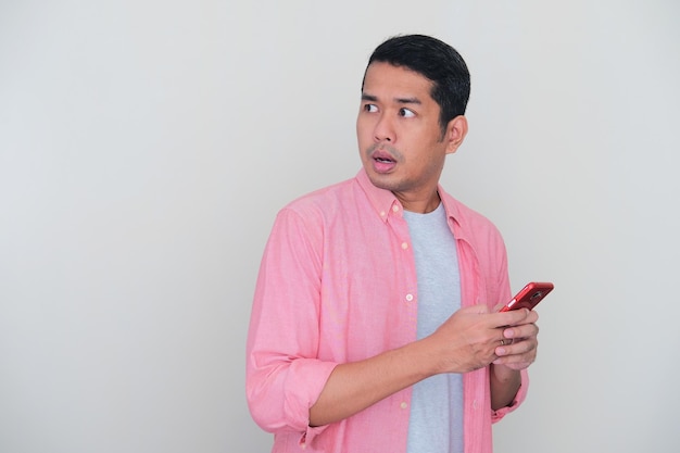 Uomo asiatico adulto che guarda indietro con espressione preoccupata mentre tiene il telefono cellulare