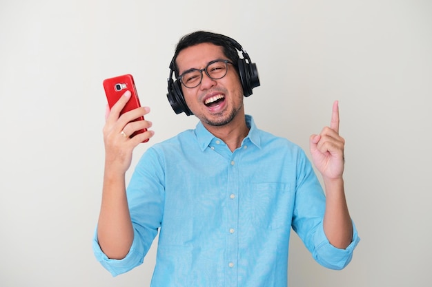 Uomo asiatico adulto che indossa l'auricolare e tiene il telefono cellulare mentre ascolta la musica