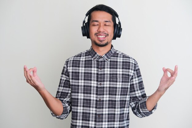 Uomo asiatico adulto che mostra facendo la posa di meditazione mentre si gode la musica usando l'auricolare