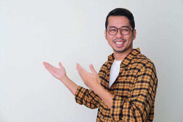 Uomo asiatico adulto che mostra qualcosa dietro il gesto con la faccia sorridente