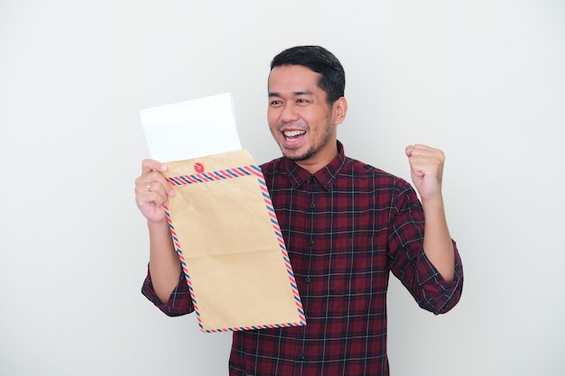 Uomo asiatico adulto che mostra un'espressione eccitata quando legge il documento dall'interno della busta della posta