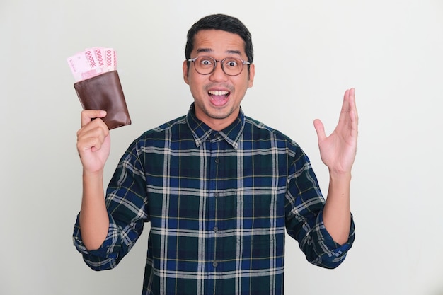 Uomo asiatico adulto che mostra un'espressione stupita mentre tiene il portafoglio pieno di soldi