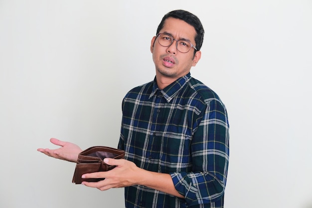 Uomo asiatico adulto che osserva la macchina fotografica con l'espressione triste mentre apre il suo portafoglio