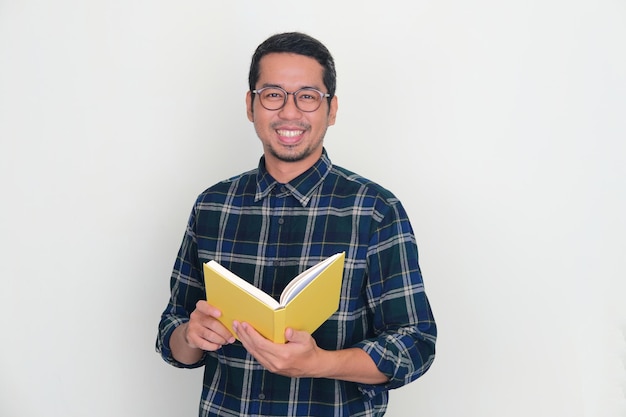 Uomo asiatico adulto che sorride alla macchina fotografica mentre tiene un libro