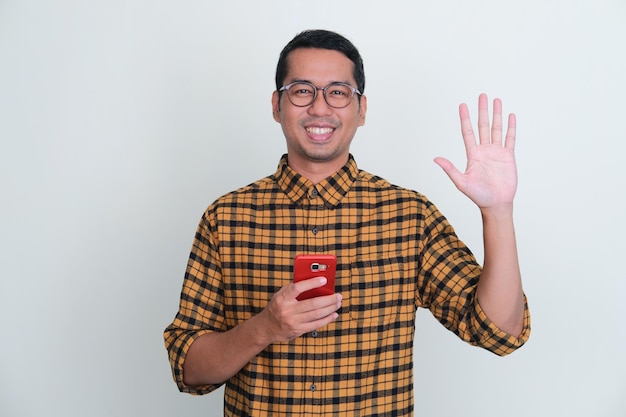 Uomo asiatico adulto che sorride e dà il segno di cinque dita mentre tiene un handphone