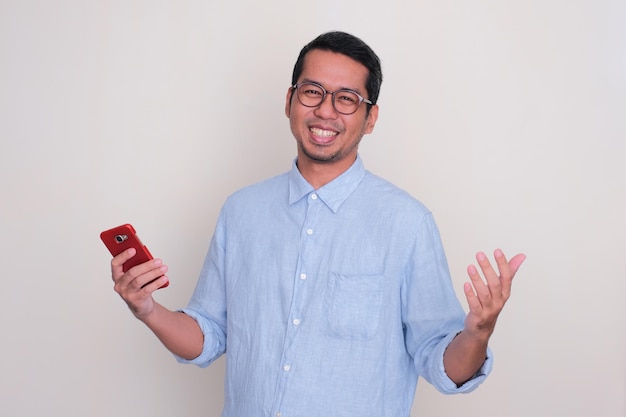 Uomo asiatico adulto che sorride felice con le braccia aperte e che tiene il telefono cellulare