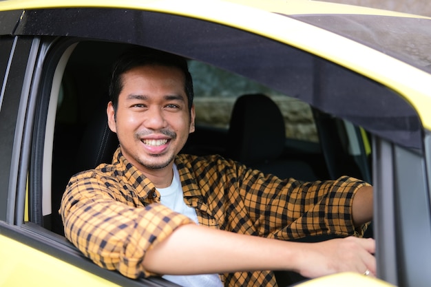 Uomo asiatico adulto che sorride felice nel sedile del conducente dell'auto