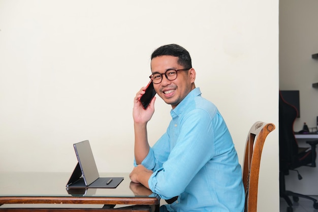 Uomo asiatico adulto che sorride fiducioso quando è seduto davanti al suo gadget tablet mobile
