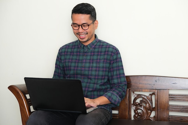 Uomo asiatico adulto seduto su una panchina mentre lavora usando il suo laptop