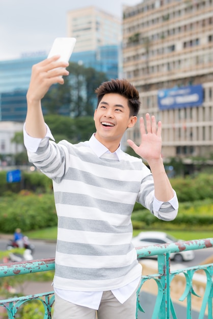 Uomo asiatico allegro che si fa selfie su uno smartphone moderno mentre si gode una piacevole passeggiata nel parco pubblico, ritratto
